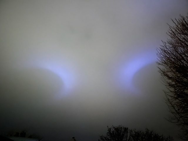 2 dark shapes above clouds with light around them and flickering